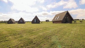 Tres cabañas de madera con techos a dos aguas en un campo cubierto de hierba.