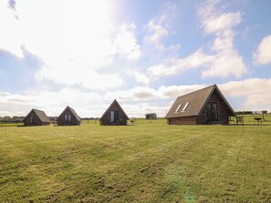 Três cabanas de madeira com telhados inclinados em um campo gramado.