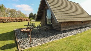 Una cabaña de madera con techo inclinado, un patio con mesa y sillas, y un sendero de grava.