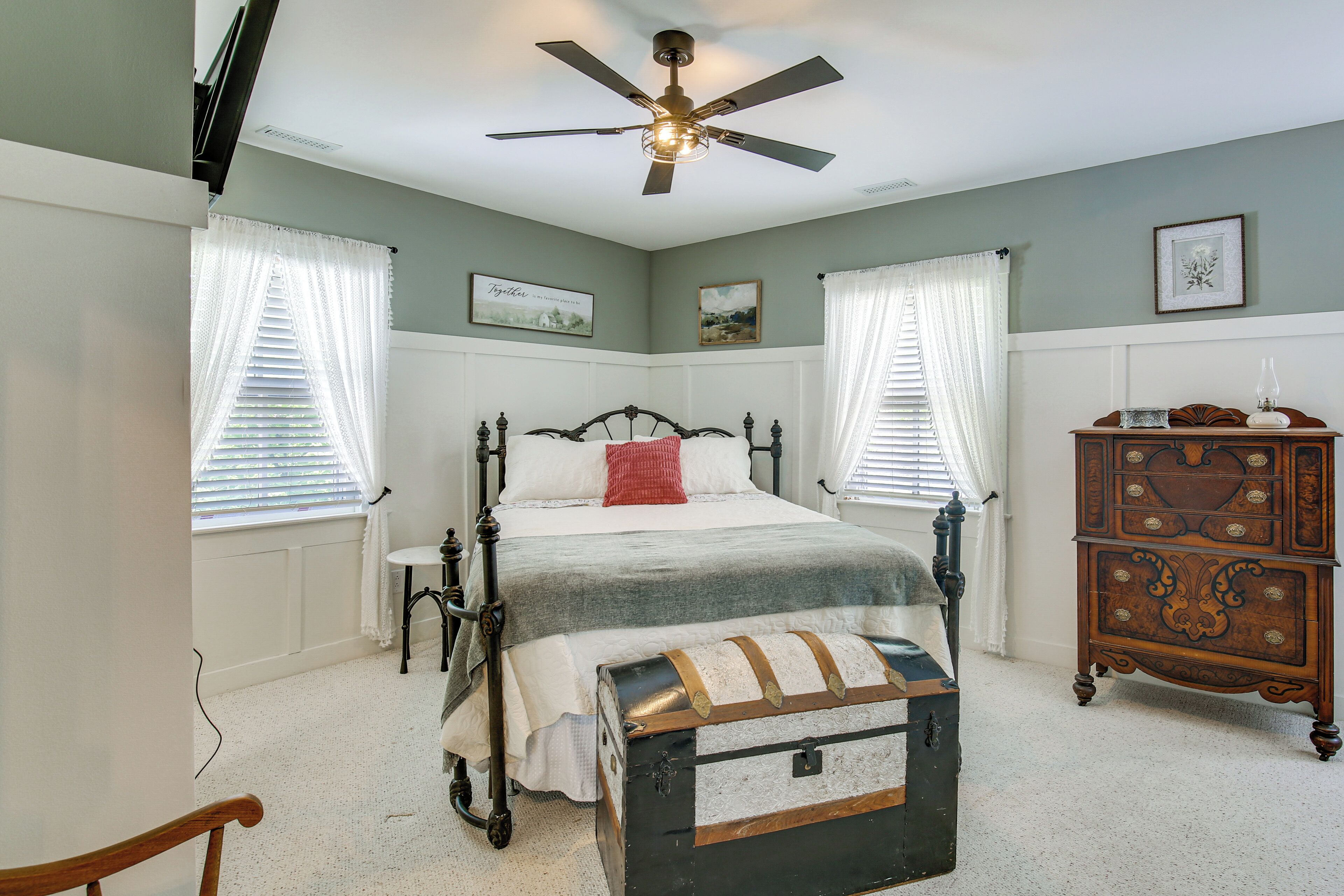A bedroom with a four-poster bed, a wooden chest, a dresser, and a ceiling fan.