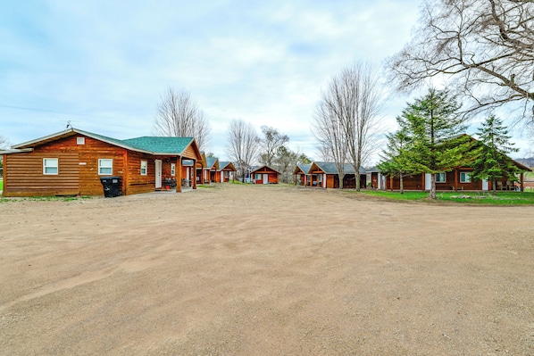 A row of log cabins with a gravel driveway and trees in the background.