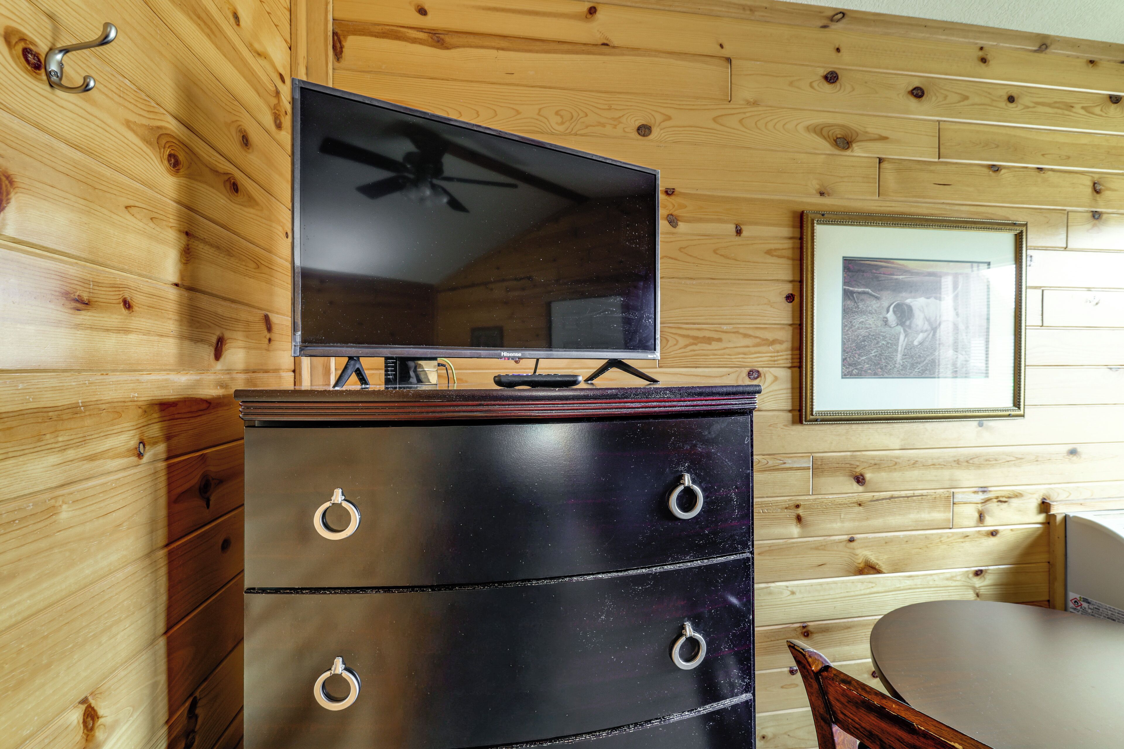 Una habitación con paneles de madera, un televisor sobre un aparador, un cuadro en la pared y una mesa de comedor.