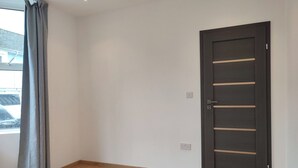A room with a wooden floor, a dark door, and a window with grey curtains. - 4 Bed Exeter City Center (New images coming soon) (Devon)