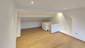 Una habitación amplia con techo inclinado, piso de madera y paredes blancas.