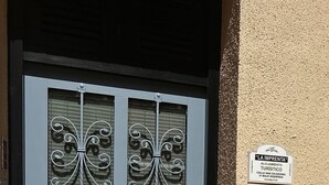 Une porte bleue ornée de panneaux de verre décoratifs, un pot de fleurs placé à côté, et une enseigne indiquant qu’il s’agit d’un hébergement touristique.