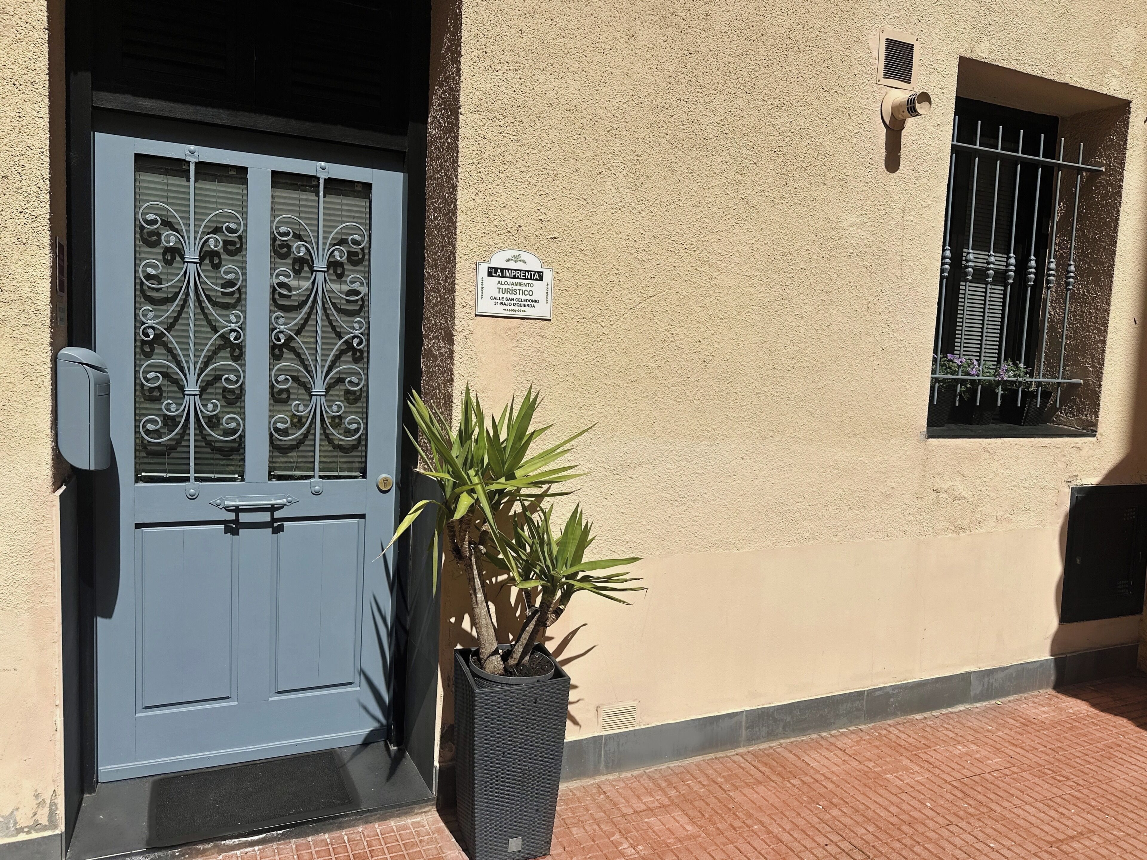 Un bâtiment avec une porte bleue, une enseigne indiquant « LA IMPRENTA », et une plante en pot.
