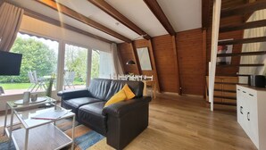 A modern living room with a black leather sofa, a glass coffee table, and a dining area with a white table and chairs. - Storchennest roof-only house: Comfortable vacation home on the North Sea in Butjadingen (Butjadingen)