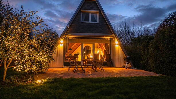 A triangular-roofed building with a patio area, outdoor seating, and a visible interior space. - Storchennest roof-only house: Comfortable vacation home on the North Sea in Butjadingen (Butjadingen)
