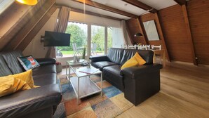 A modern loft-style living room with a black leather sofa, a coffee table, and a TV mounted on the wall. - Storchennest roof-only house: Comfortable vacation home on the North Sea in Butjadingen (Butjadingen)