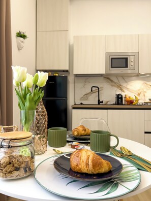 A breakfast setting with a croissant, a jar of cereal, a vase with flowers, and a microwave in a modern kitchen.