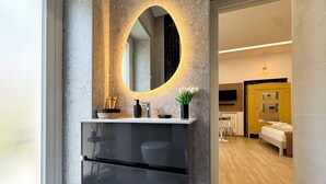 A modern bathroom with a granite countertop, a black sink, and a mirror with a circular light.
