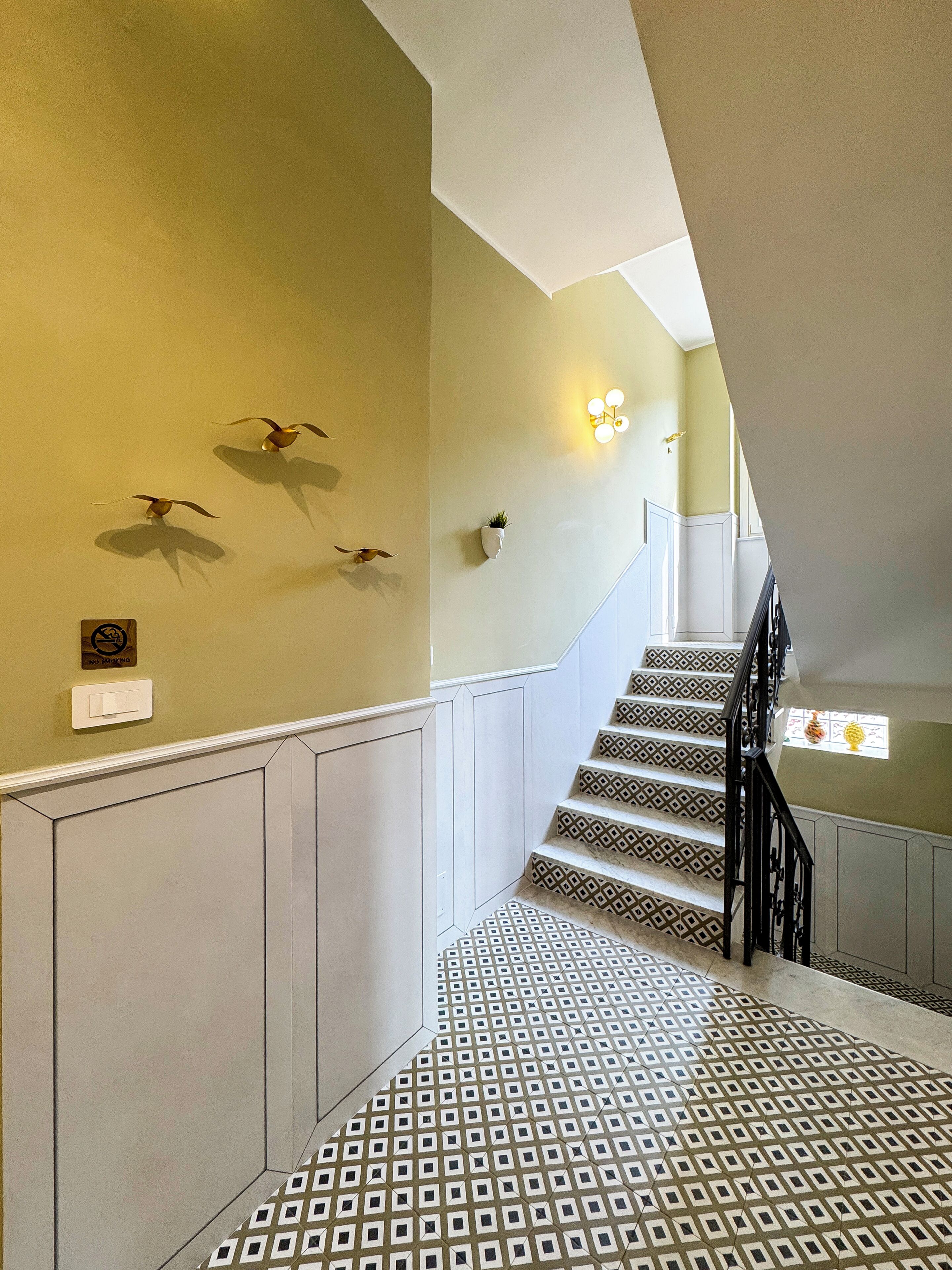 Una escalera con peldaños decorados, una lámpara de pared y obras de arte en la pared.