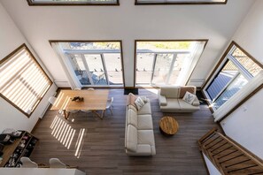A spacious living area with a dining table, sofas, and a coffee table. Large windows provide ample natural light and views of the outdoors. - Clematites | Private Spa & Games | Nature & Lake (Matawinie Regional County Municipality)