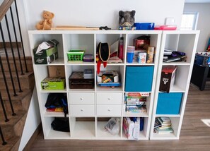 Ein weißes Regal mit verschiedenen Gegenständen, darunter Brettspielen, Büchern und Aufbewahrungsboxen.
