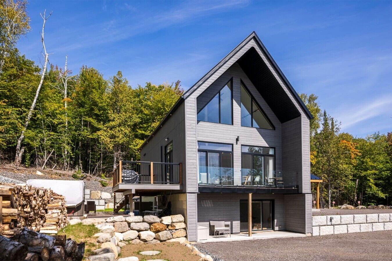 A modern two-story house with a balcony, large windows, and a stone foundation.