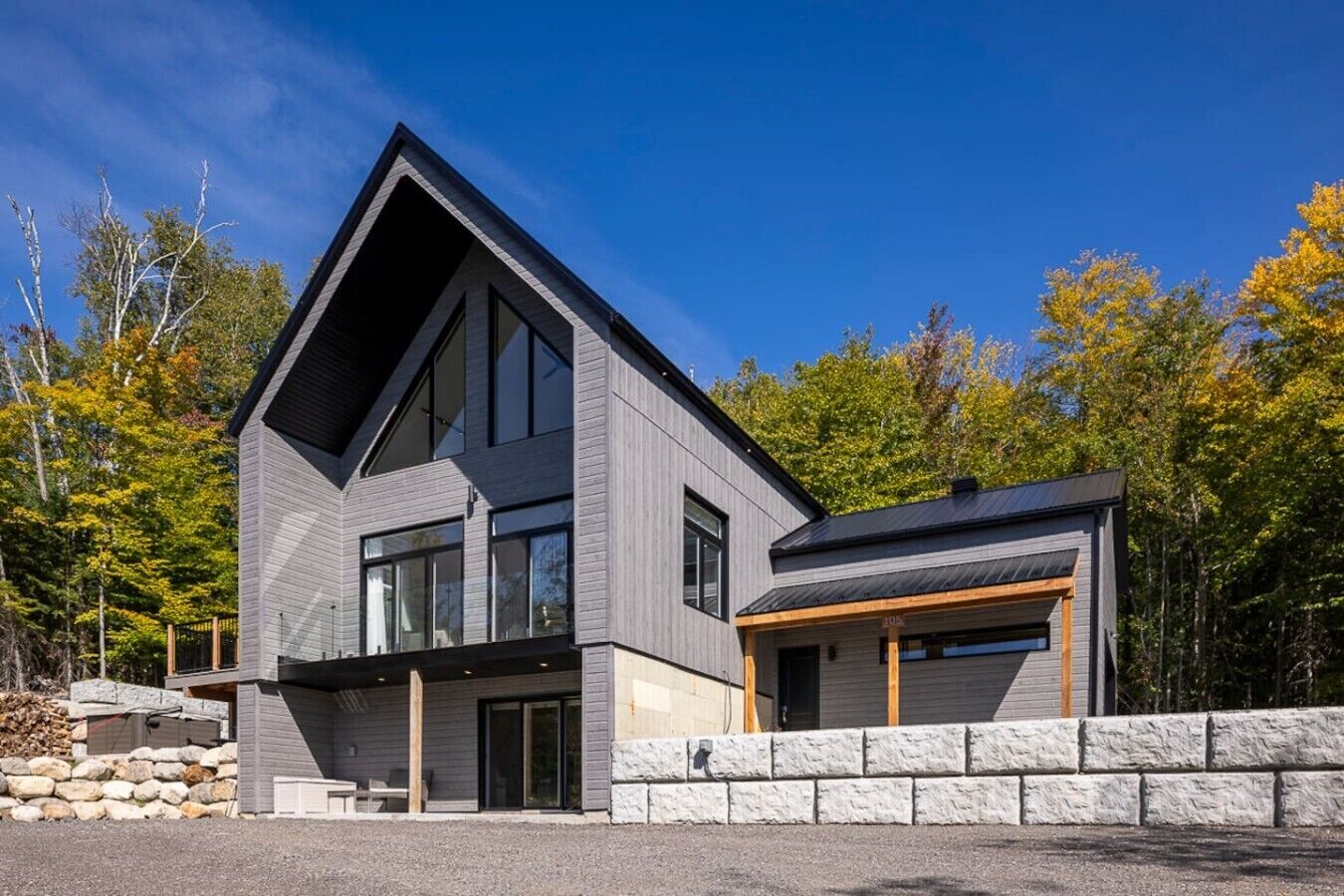 Une maison moderne à deux étages, dotée d’un garage, de grandes fenêtres et d’un mur de soutènement en pierre.