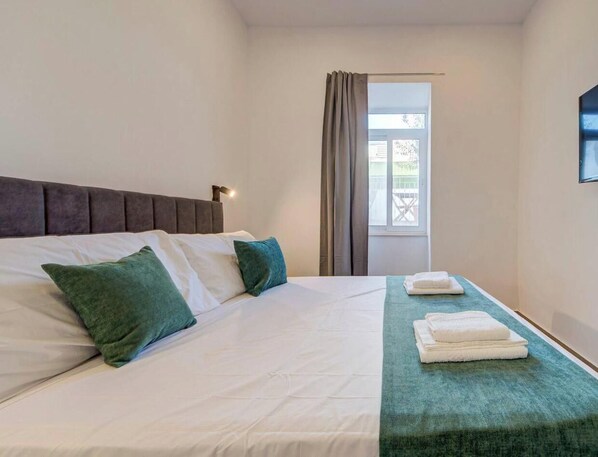A hotel room with a bed, pillows, a window, and a towel rack. - Charming 1BR home w/Balcony | Ferry 5 Min Away (Bormla)
