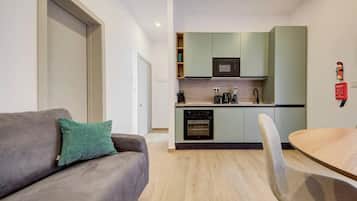 Une cuisine moderne équipée d’un four à micro-ondes, d’un four et d’un évier, un canapé gris avec un coussin vert et une table à manger en bois avec une chaise.