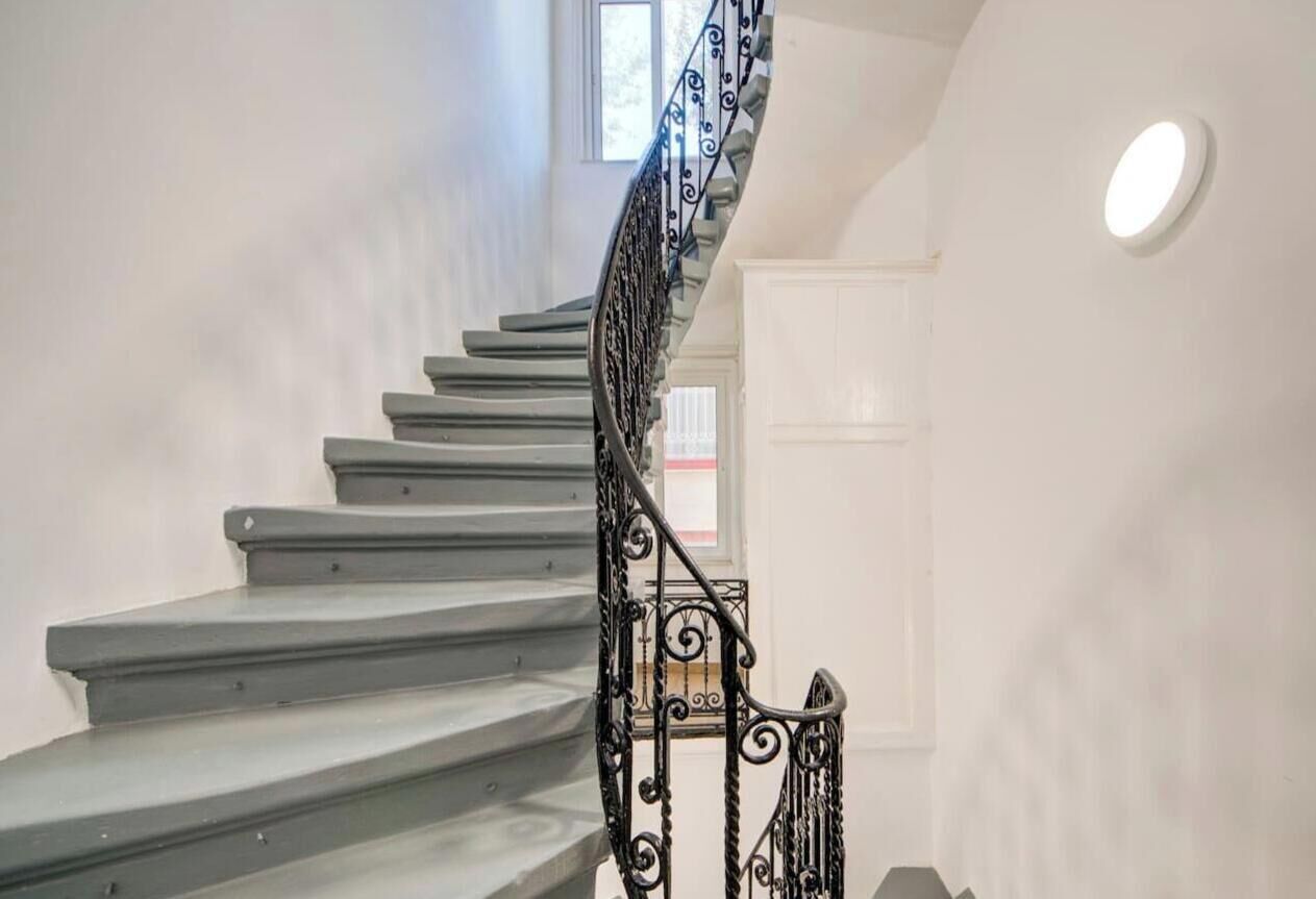 Un escalier avec une rampe en métal noir et un mur blanc.