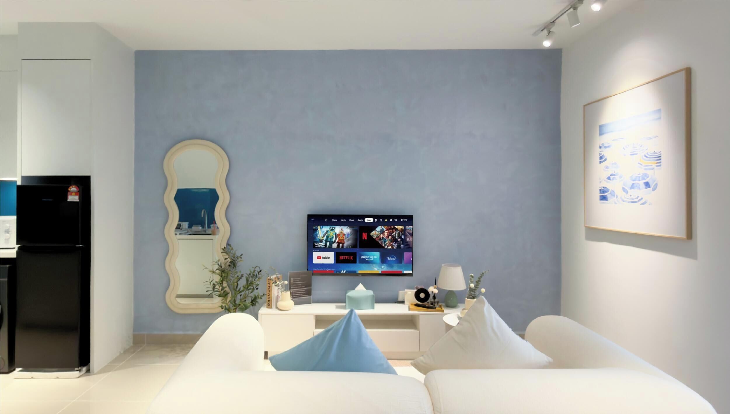A modern living room with a flat-screen TV, a white sofa, a mirror, and a framed picture on the wall.