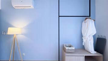 A room with a lamp, a robe hanging on a rack, a bedside table with a small box, and a wall-mounted air conditioner.