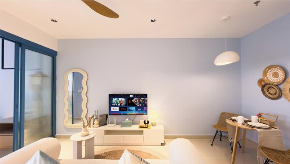 Una sala moderna con un televisor de pantalla plana, un sofá, una mesa de comedor con sillas y un espejo grande.
