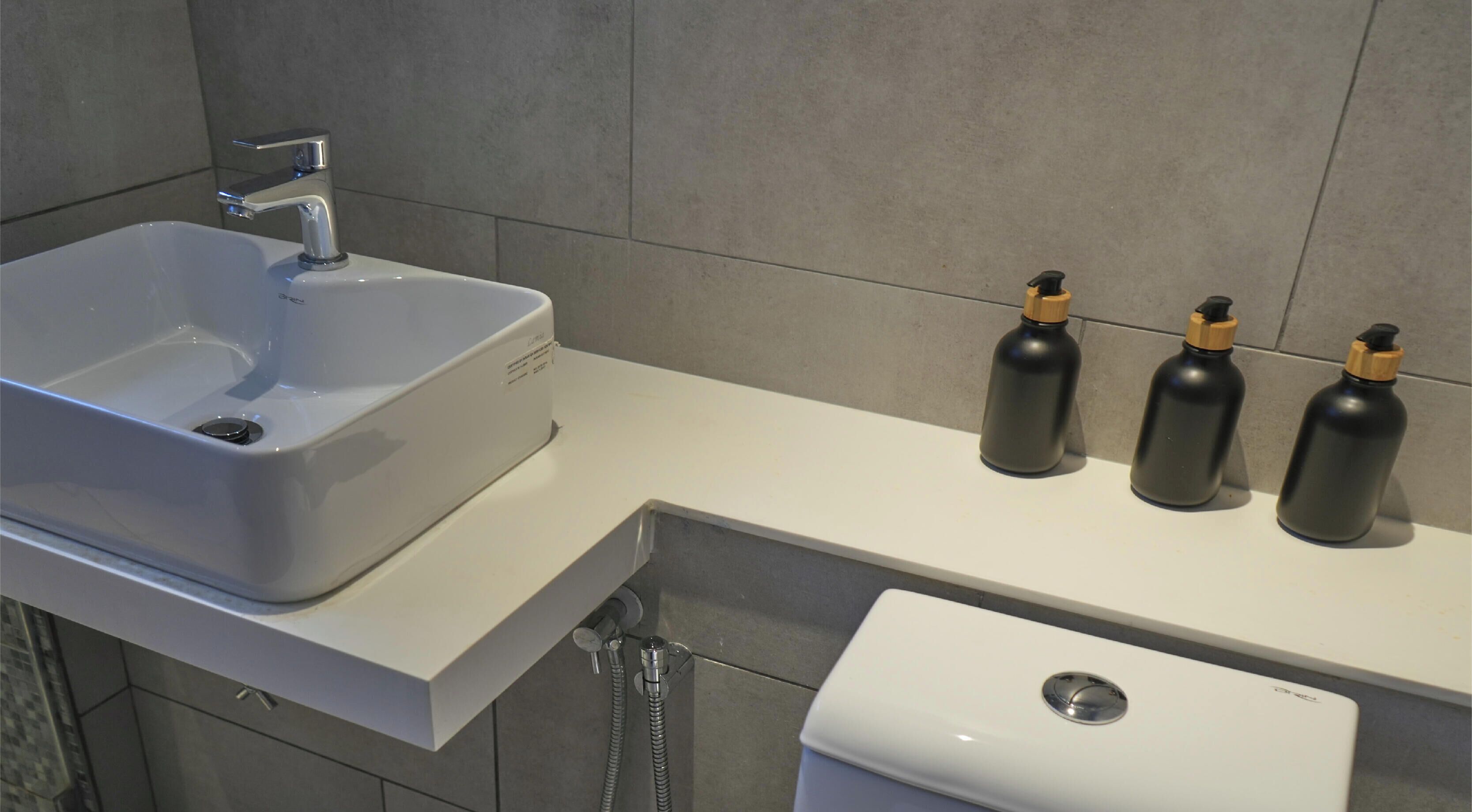 A bathroom with a white sink, a toilet, and three black bottles on the counter.