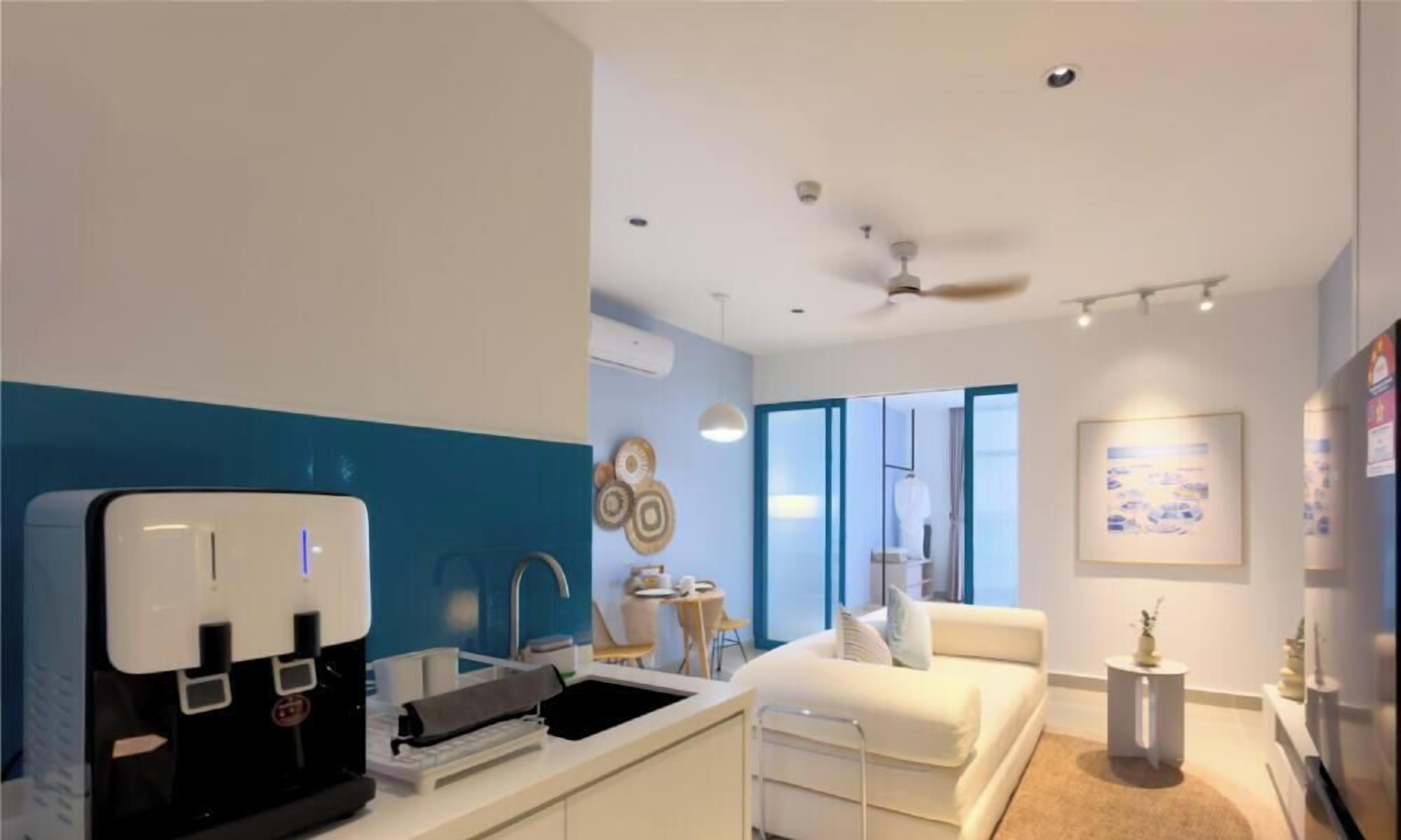 A modern hotel room with a kitchenette, a bed, a small seating area, and a view through the window.