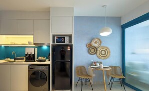 Uma cozinha moderna com cafeteira, máquina de lavar louça e frigorífico. Possui uma área de refeições com mesa e cadeiras, e uma parede com pratos decorativos.