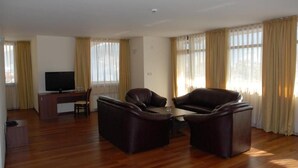 Una sala de estar con piso de madera, un escritorio con computadora, dos sofás de cuero y un televisor.