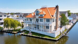 Ein Haus am Wasser mit einem markanten Schornstein, mehreren Balkonen und einer anlegenden Mole.