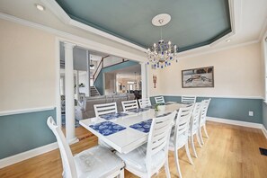 Un comedor con una mesa y sillas blancas, una araña y una escalera que lleva a otra habitación.
