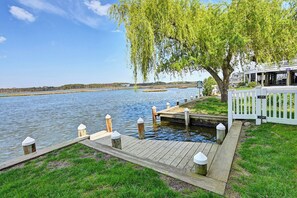 Eine hölzerne Anlegestelle erstreckt sich über ruhiges Wasser, ein weißer Zaun und ein Baum mit überhängenden Ästen.