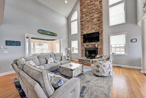Ein Wohnzimmer mit Ecksofa, Couchtisch, gemustertem Sessel, Kamin aus Stein und Wand-Fernseher.