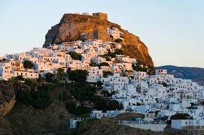 A densely packed hillside settlement with white buildings, a prominent rocky hill, and a fortified structure on top.