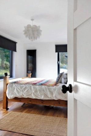 Um quarto com cama, janela, porta e luminária pendente.