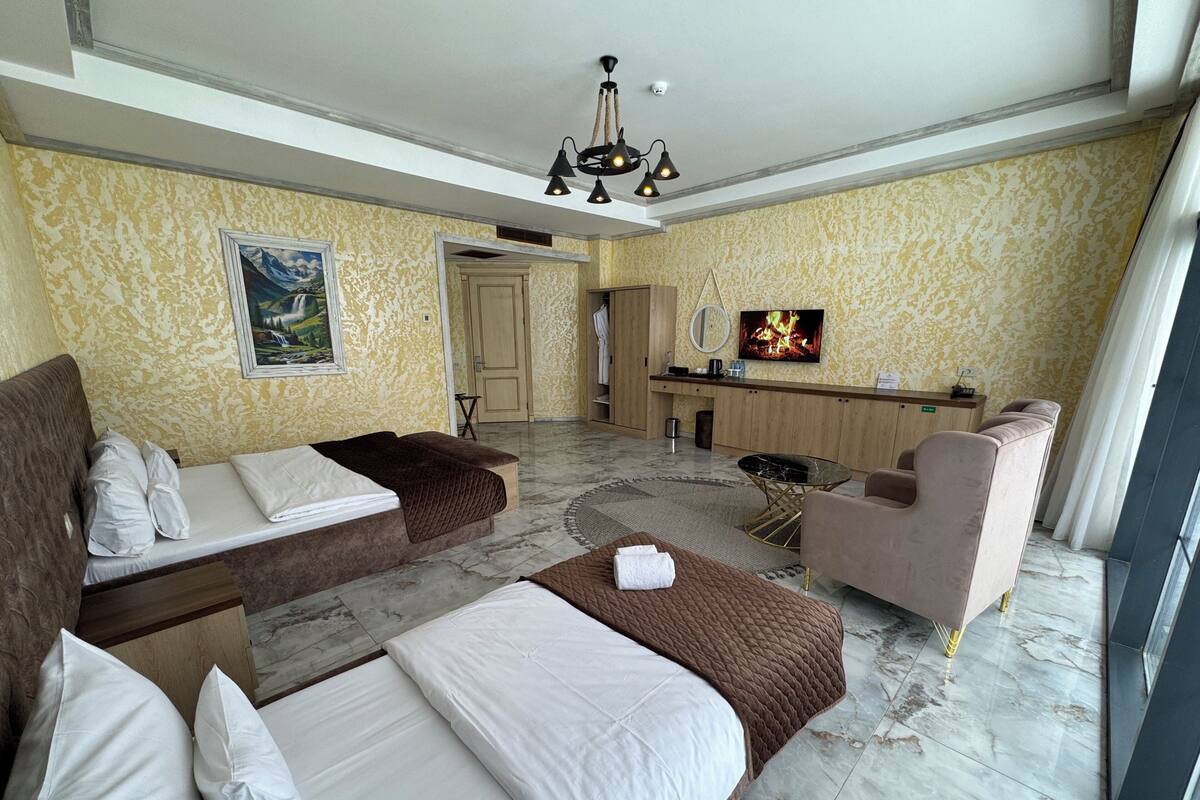 A hotel room with two beds, a sofa, a chair, a TV, a desk, and a mirror.