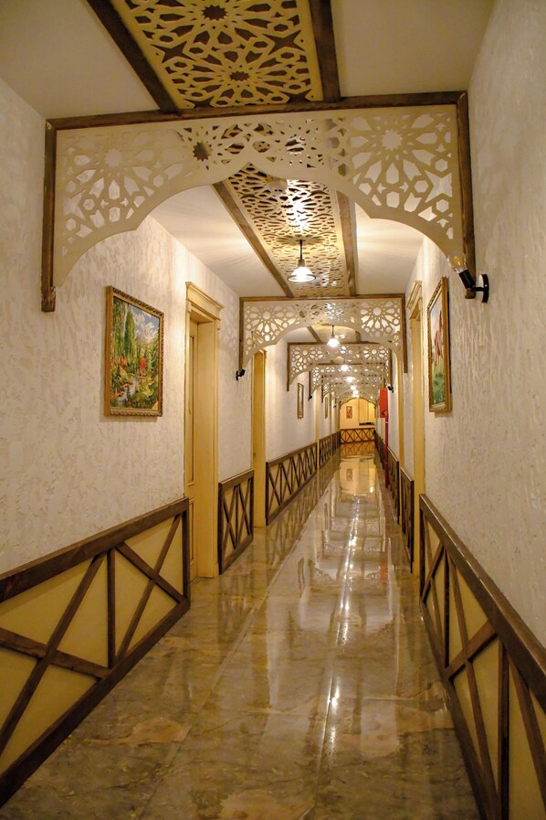 A hallway with a marble floor, wooden railings, and decorative ceiling patterns.
