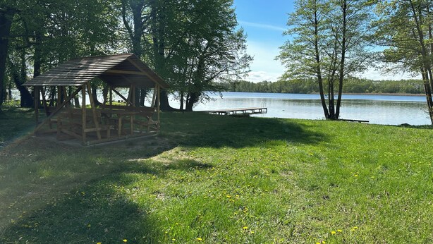 A wooden gazebo with benches, a dock extending into a lake, surrounded by trees. - Top location on the lake - Charming yellow bungalow with terrace & lake view (Neuruppin)