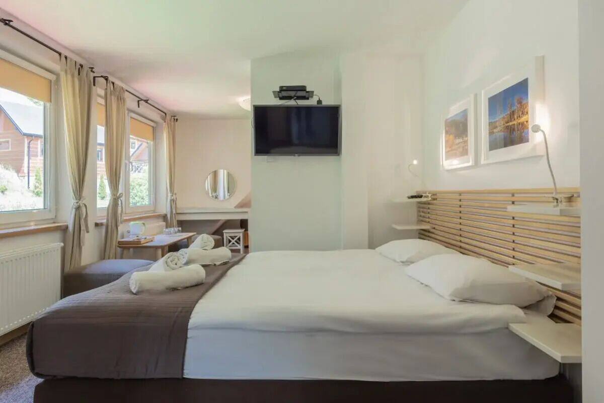 Une chambre d’hôtel avec un grand lit, un téléviseur fixé au mur, un bureau avec une chaise et une fenêtre avec des rideaux.