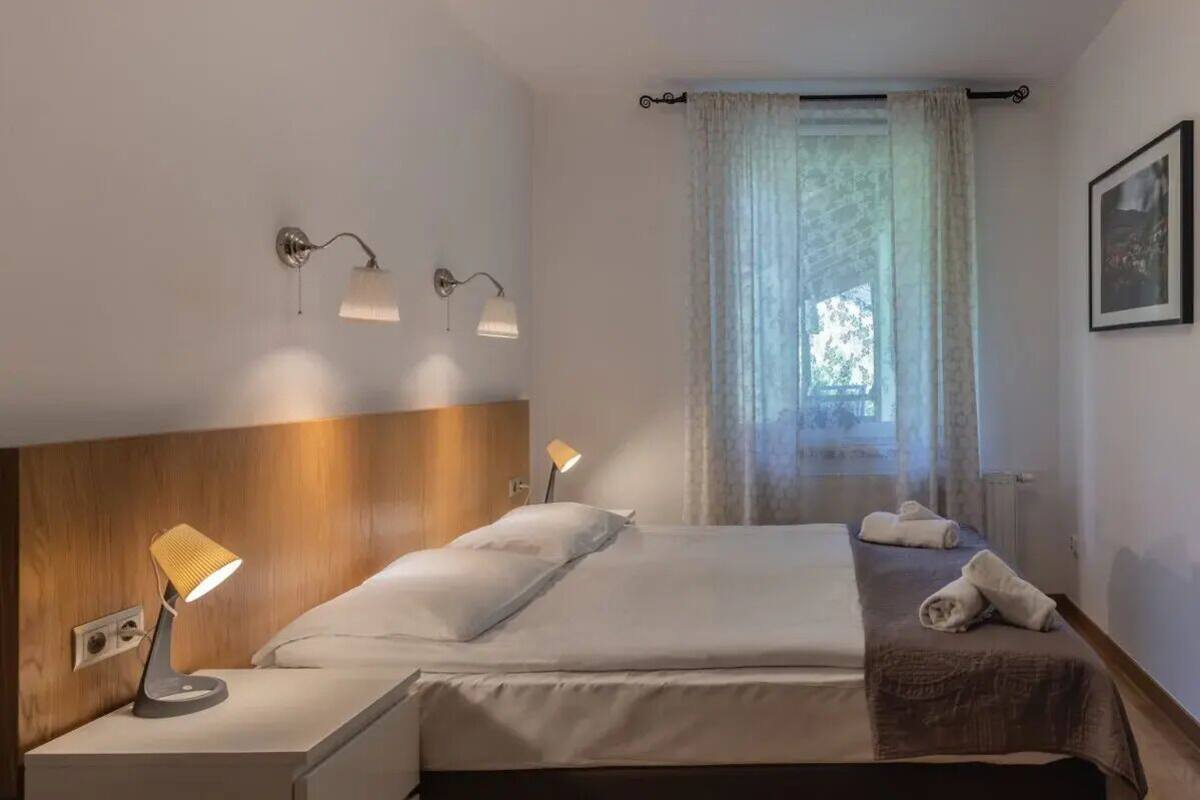 Une chambre d’hôtel avec un lit, deux lampes de chevet, une fenêtre avec des rideaux et un tableau encadré au mur.