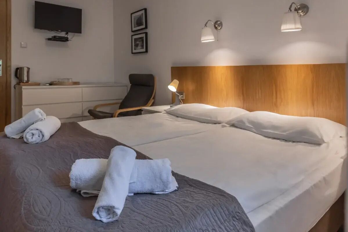 A hotel room with a large bed, a flat-screen TV, a desk with a chair, and two wall-mounted lamps.
