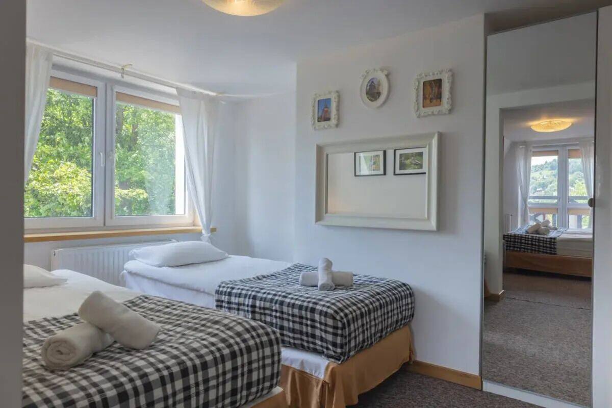 Une chambre d’hôtel avec deux lits, une grande fenêtre et un miroir qui reflète la pièce.