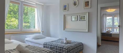 A hotel room with two beds, a large window, and a mirror reflecting the room.
