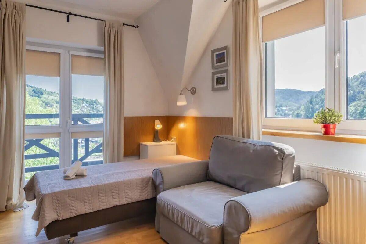Une chambre à coucher comprenant un lit, un canapé, une table de chevet, une lampe, une fenêtre avec vue et une plante en pot.