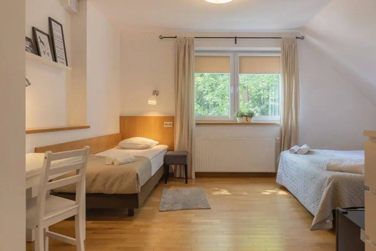 Une chambre avec deux lits, un bureau, une chaise, un radiateur et une fenêtre avec des rideaux.