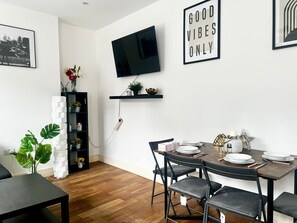 A modern dining area with a round table, black chairs, and a mounted TV. - 2BR Apartment in the heart of Streatham High road (London)