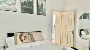 Een keurig opgemaakt bed met witte lakens, een zwart hoofdbord en een spiegel aan de muur.