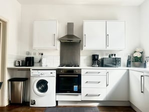 A compact kitchen with white cabinets, a washing machine, a microwave, a toaster, and a coffee maker. - 2BR Apartment in the heart of Streatham High road (London)