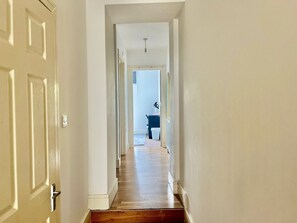 A hallway with wooden flooring, white walls, and a door on the left. - 2BR Apartment in the heart of Streatham High road (London)